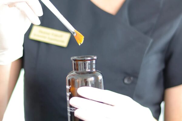 Behandler dypper en pensel i kemisk peel fra en brun glasflaske